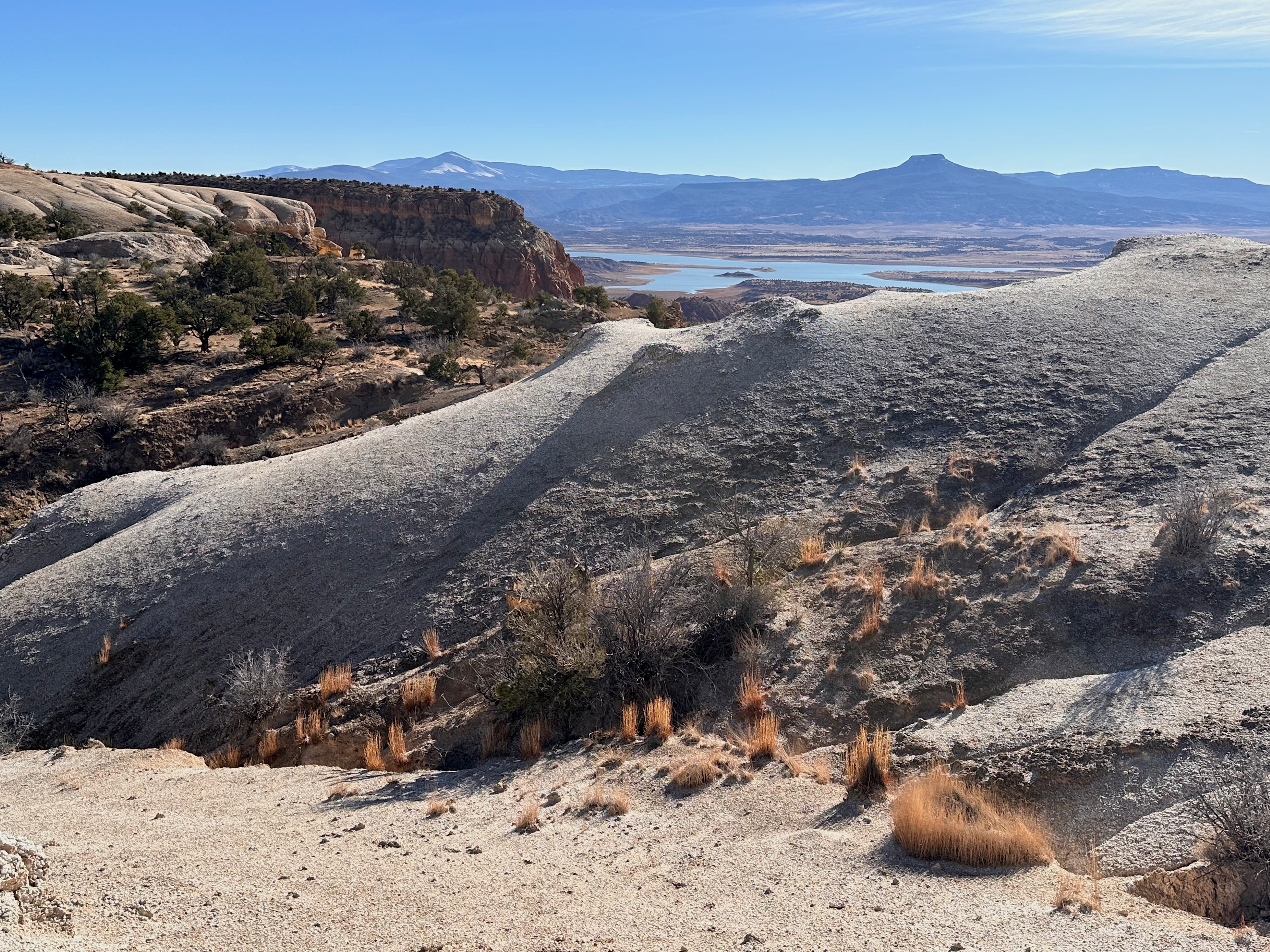 Pale eroded hills above a reservoir, with a flat-topped mesa on the horizon, northern New Mexico.